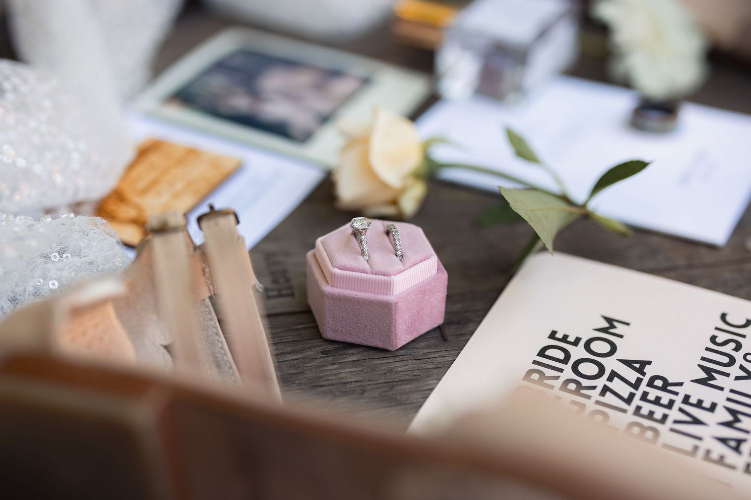 A pink hexagonal ring box sits among papers and stationery items on a wooden desk with a small green plant leaf.