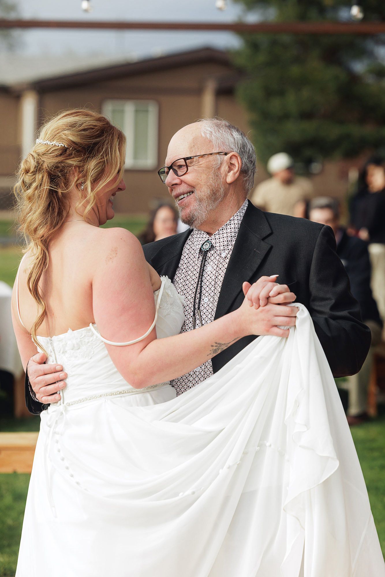 Bride and elderly man share emotional father-daughter dance outdoors at wedding reception.