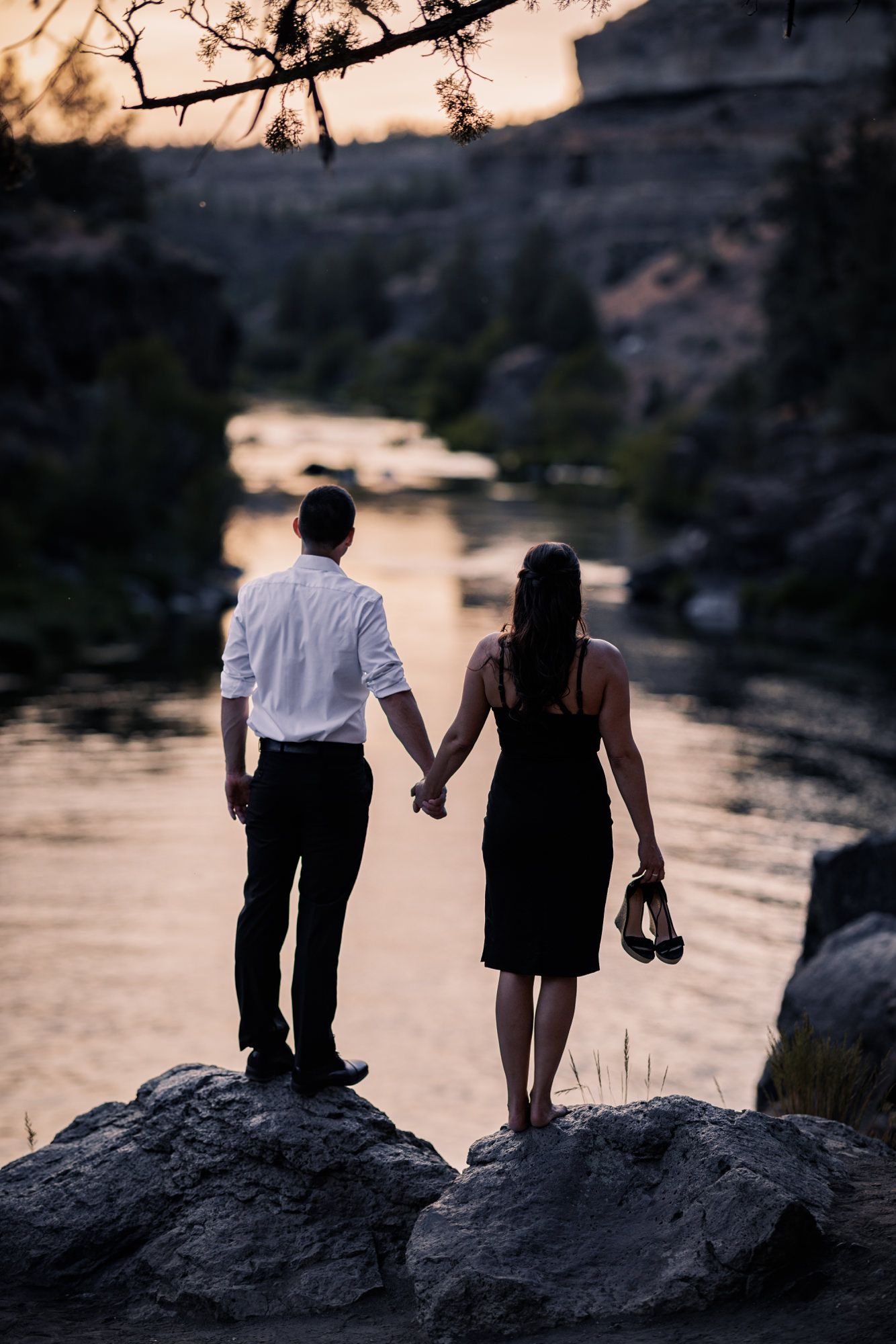 Silhouette of a couple walking along rocky riverbank at sunset in romantic nature setting.