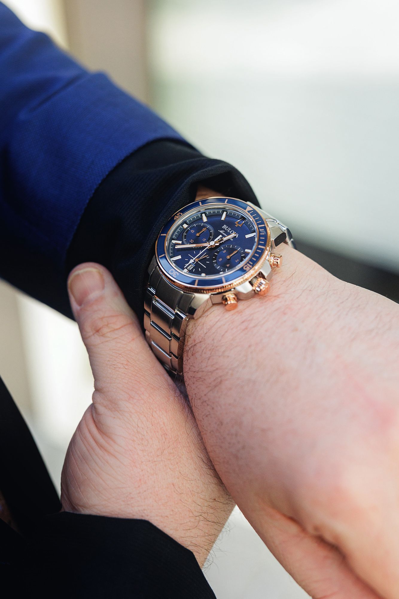 Close-up view of a blue-faced chronograph watch with stainless steel bracelet shown from multiple angles on wrist.