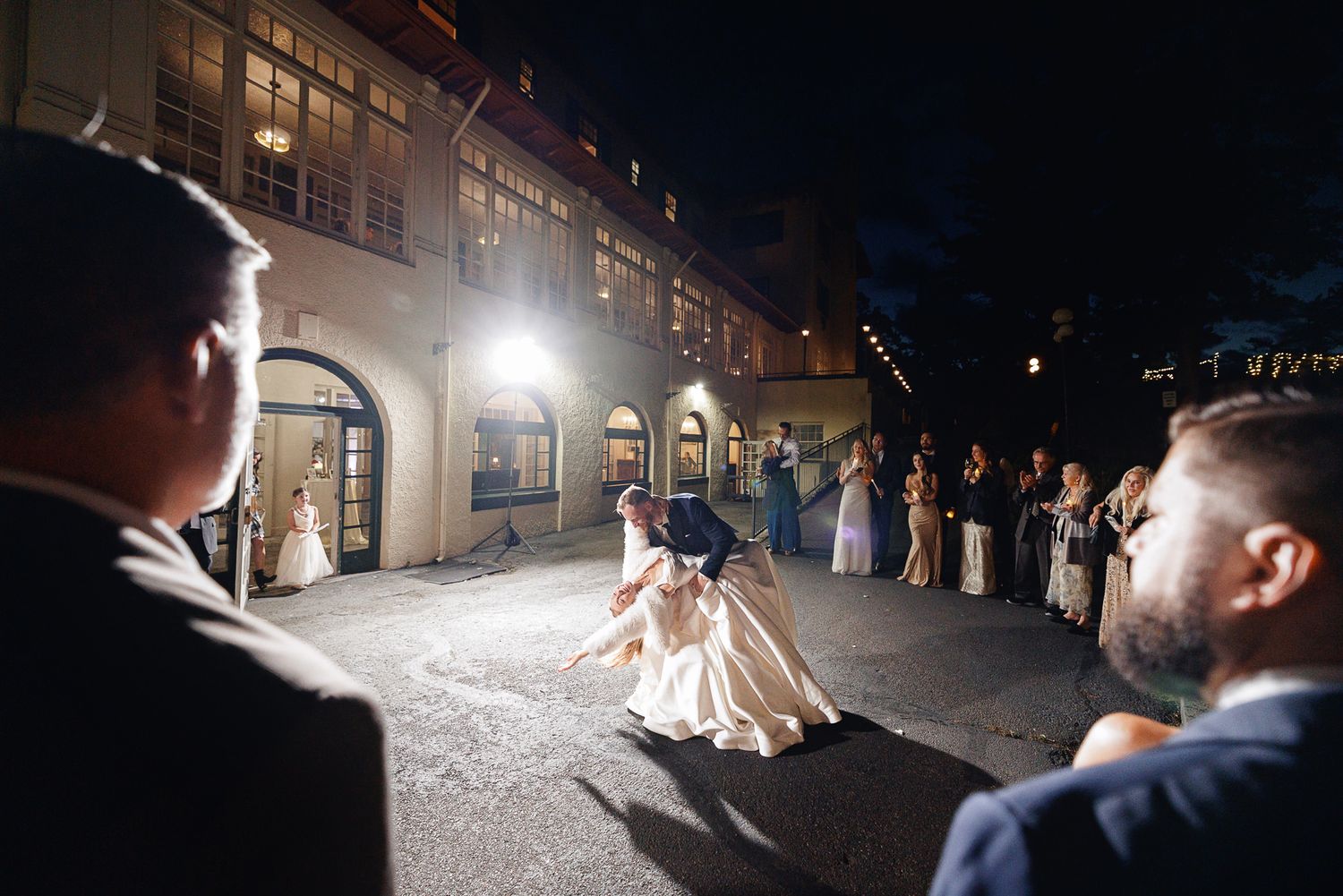 Bride and groom share first dance outdoors at night with wedding guests watching at elegant venue.
