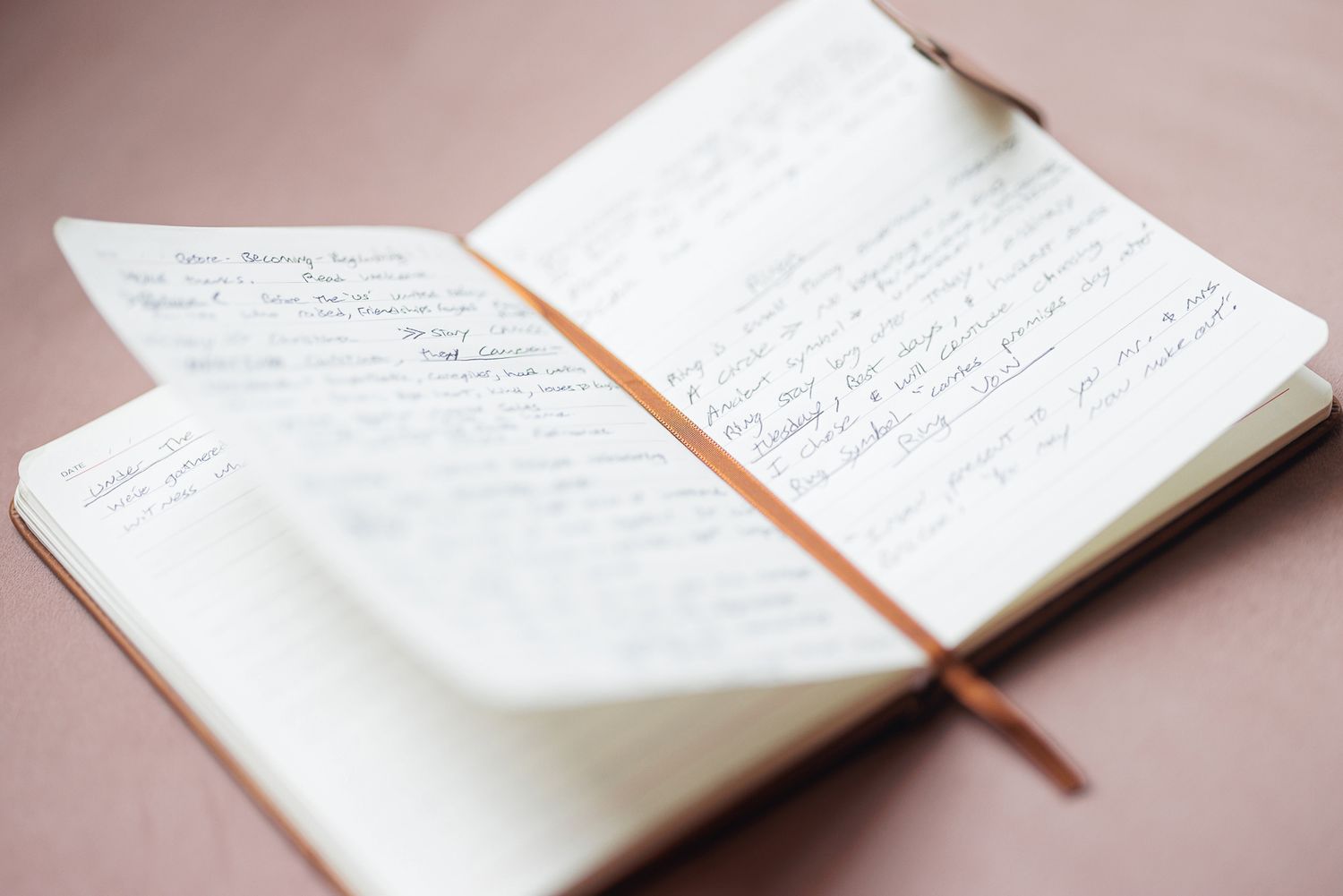 Open handwritten journal notebook with elastic band closure on a pink surface.