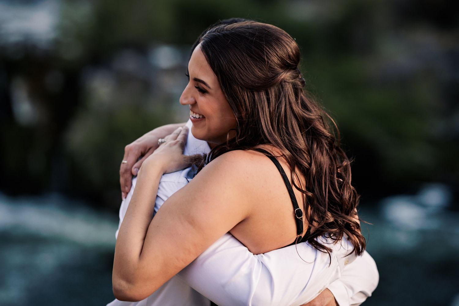A couple embraces in an intimate moment during an outdoor photoshoot with blurred natural background.