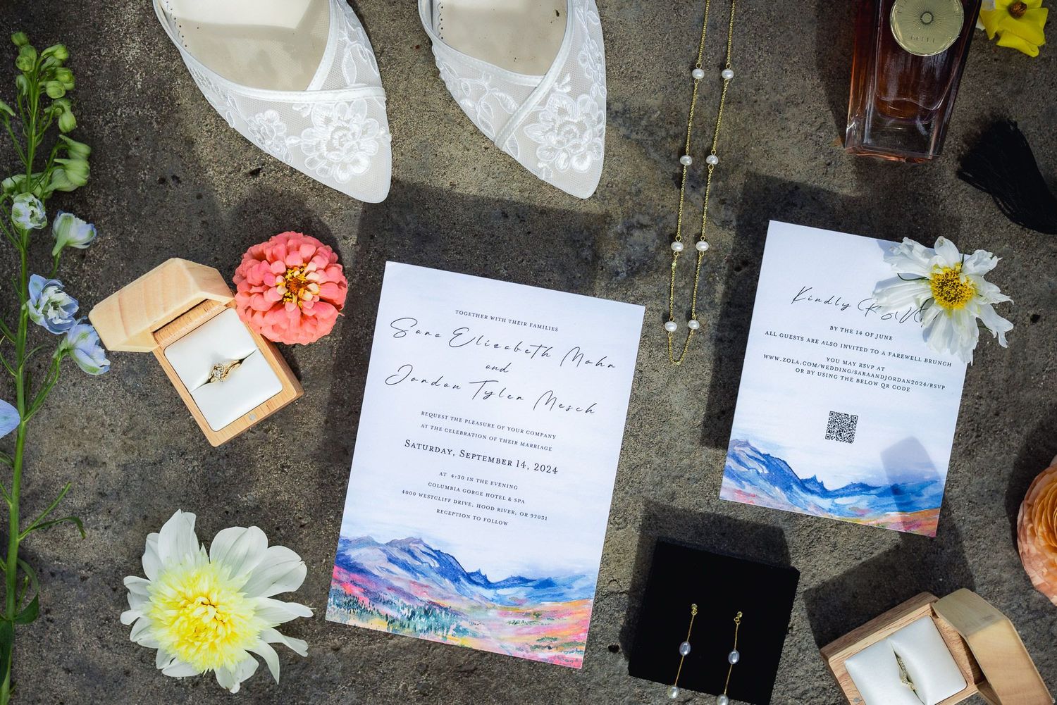Wedding details flat lay with invitations, white shoes, jewelry box, and yellow flowers arranged on stone surface.
