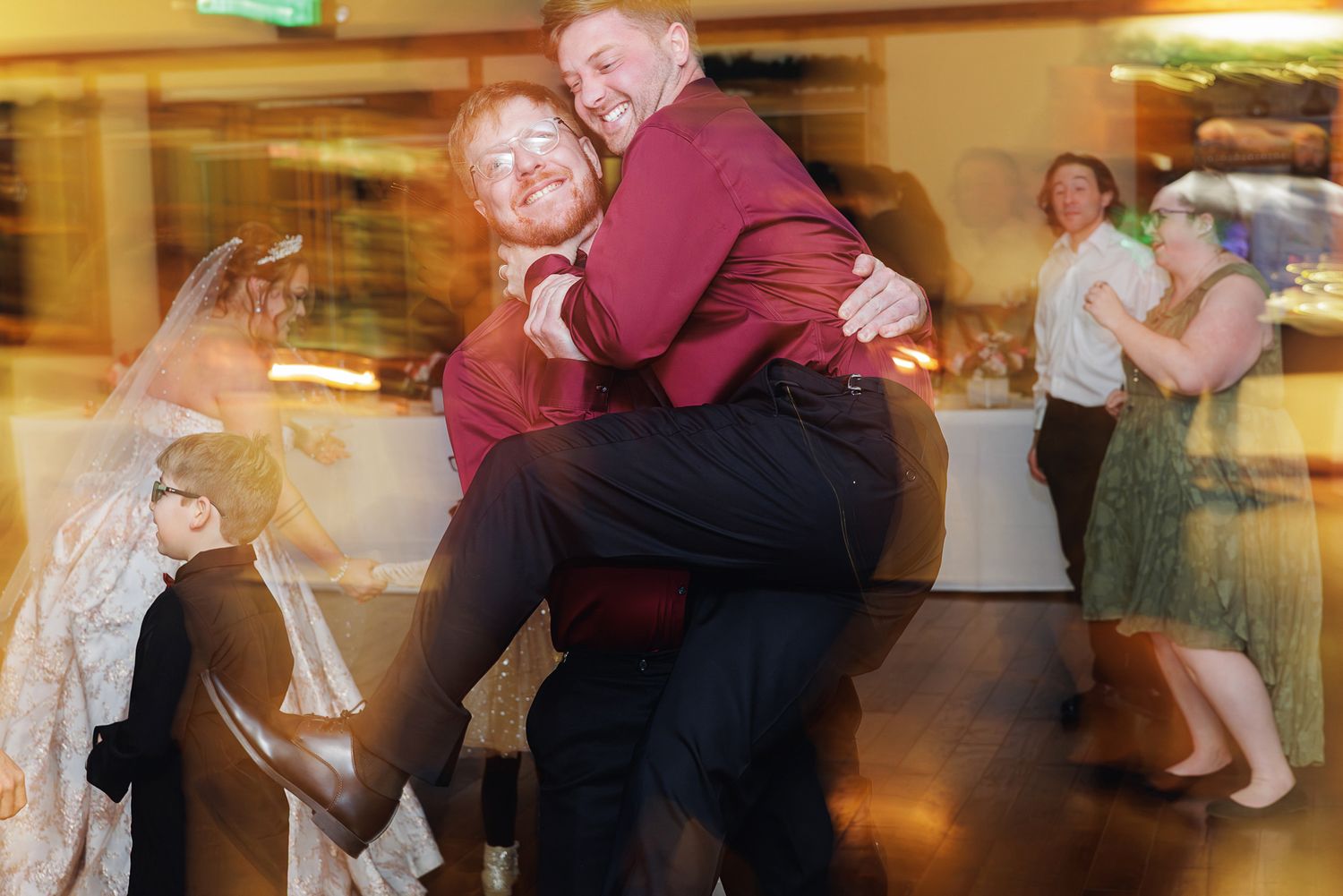 Wedding guests dancing and celebrating at a reception with burgundy and pink decor.