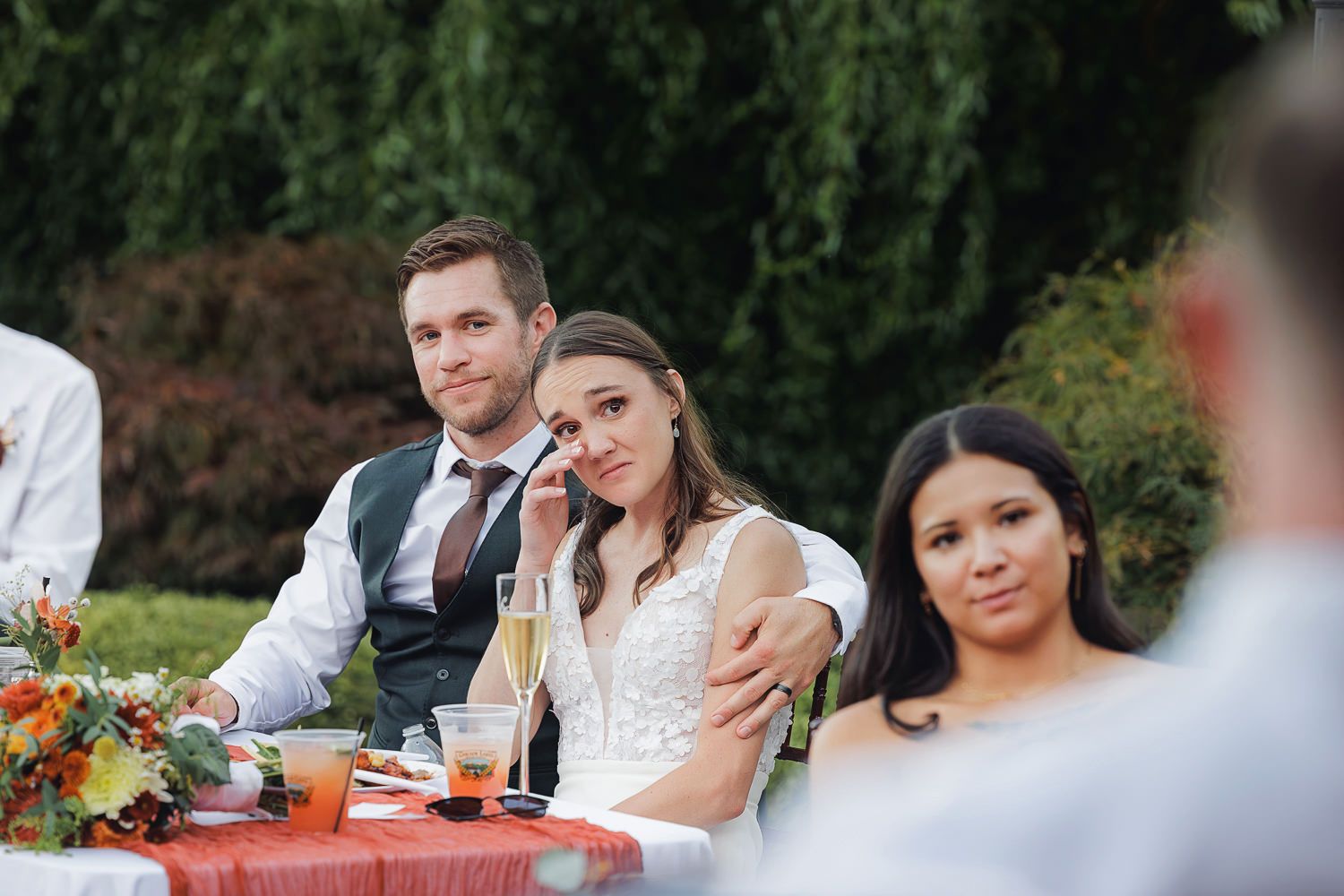 Wedding guests enjoy an outdoor reception dinner at decorated tables with floral centerpieces.