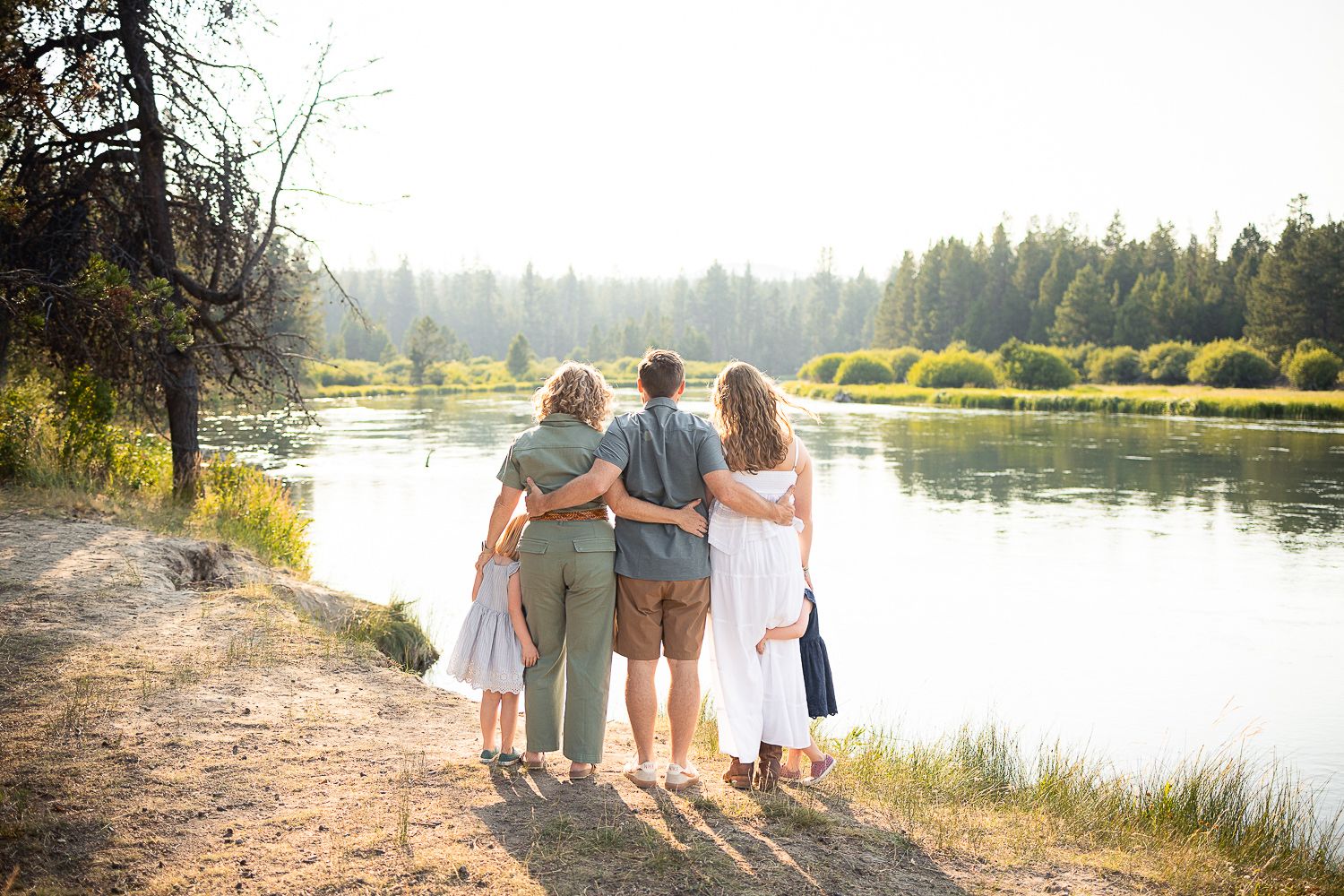 Family in coordinating white outfits walks along a scenic lakeside path during golden hour.