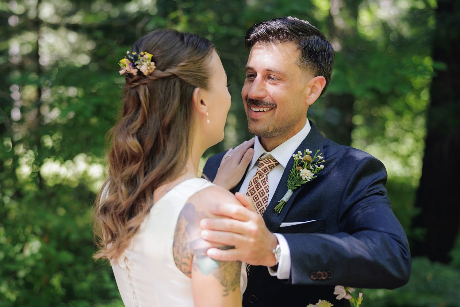 Happy couple embrace and smile together during outdoor wedding ceremony in lush green forest setting.