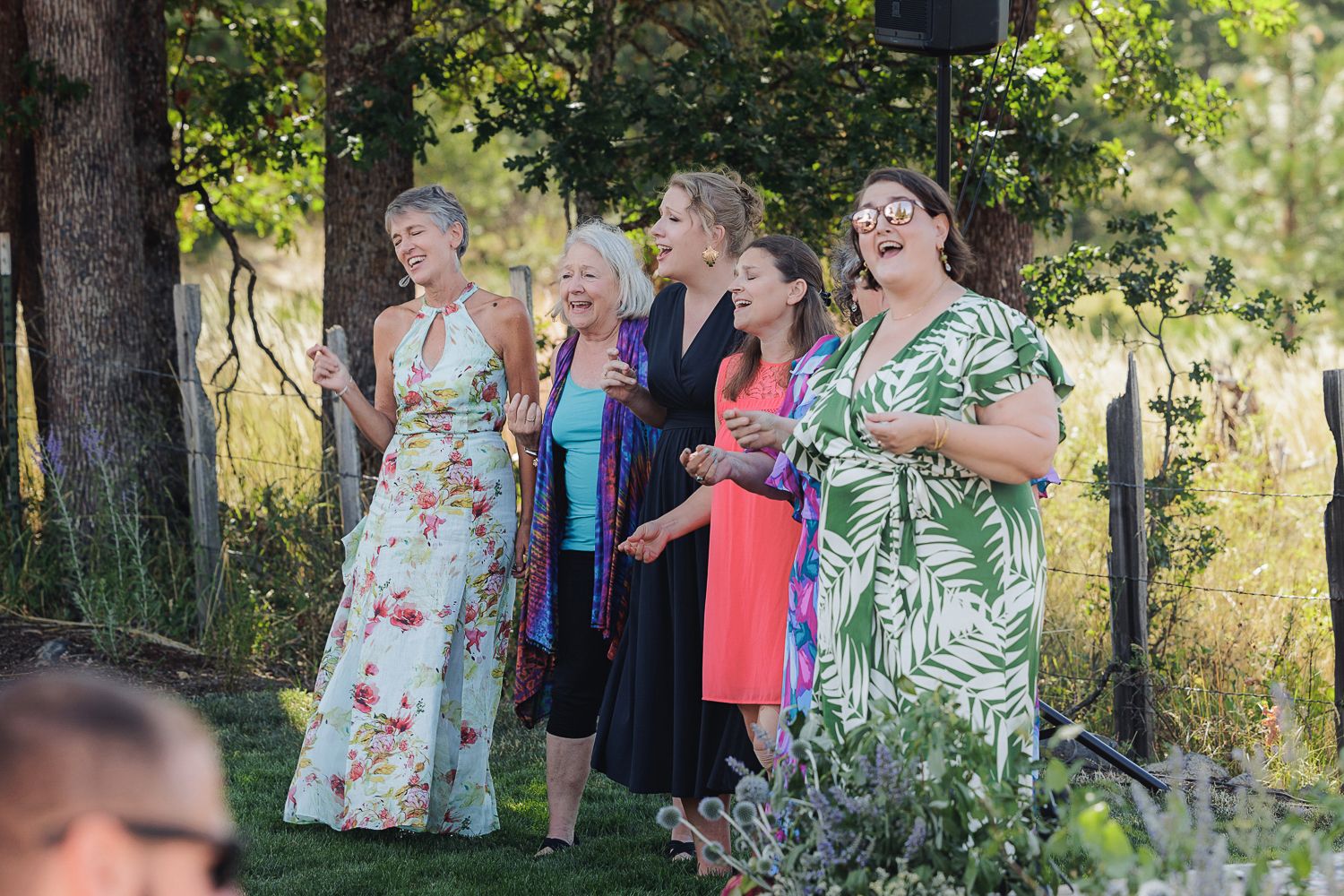 A group of guests enjoying themselves outdoors at a summer event, with trees and sunshine in the background.