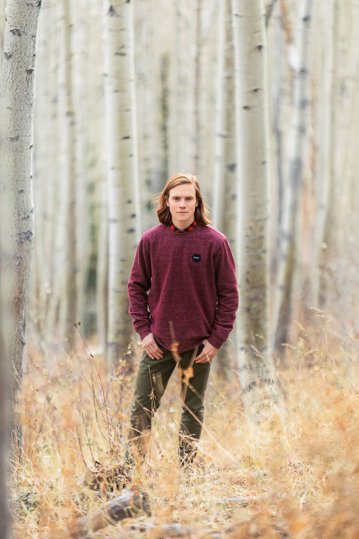 Person in burgundy sweater standing among bare aspen trees in autumn.