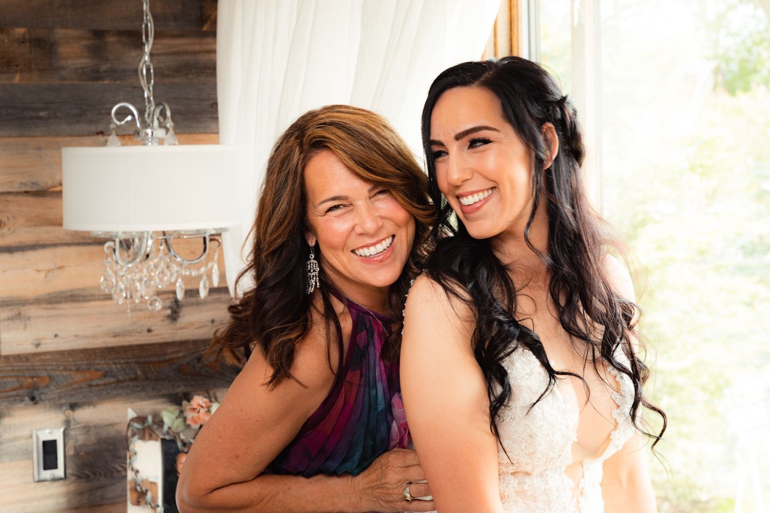 Two people smile together in an intimate pose at a rustic venue with wood walls and chandelier lighting.