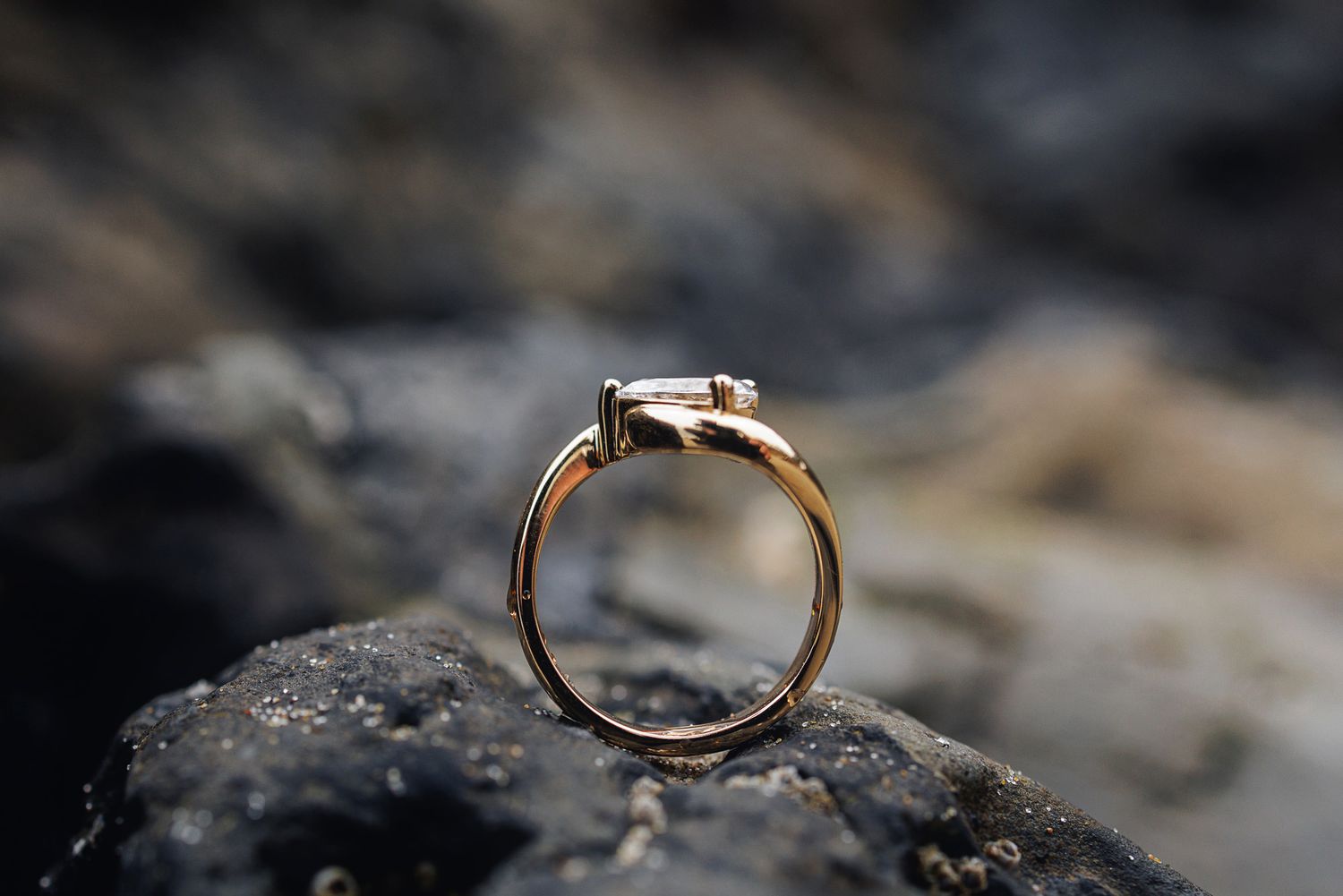 Gold engagement ring with a dark gemstone balanced upright on a rocky surface.