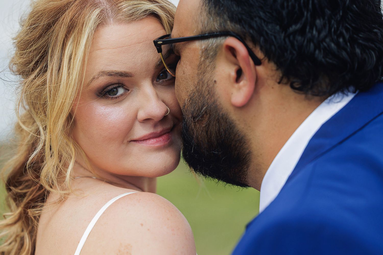 A bride and groom share an intimate moment, with the groom whispering to the smiling blonde bride in wedding attire.
