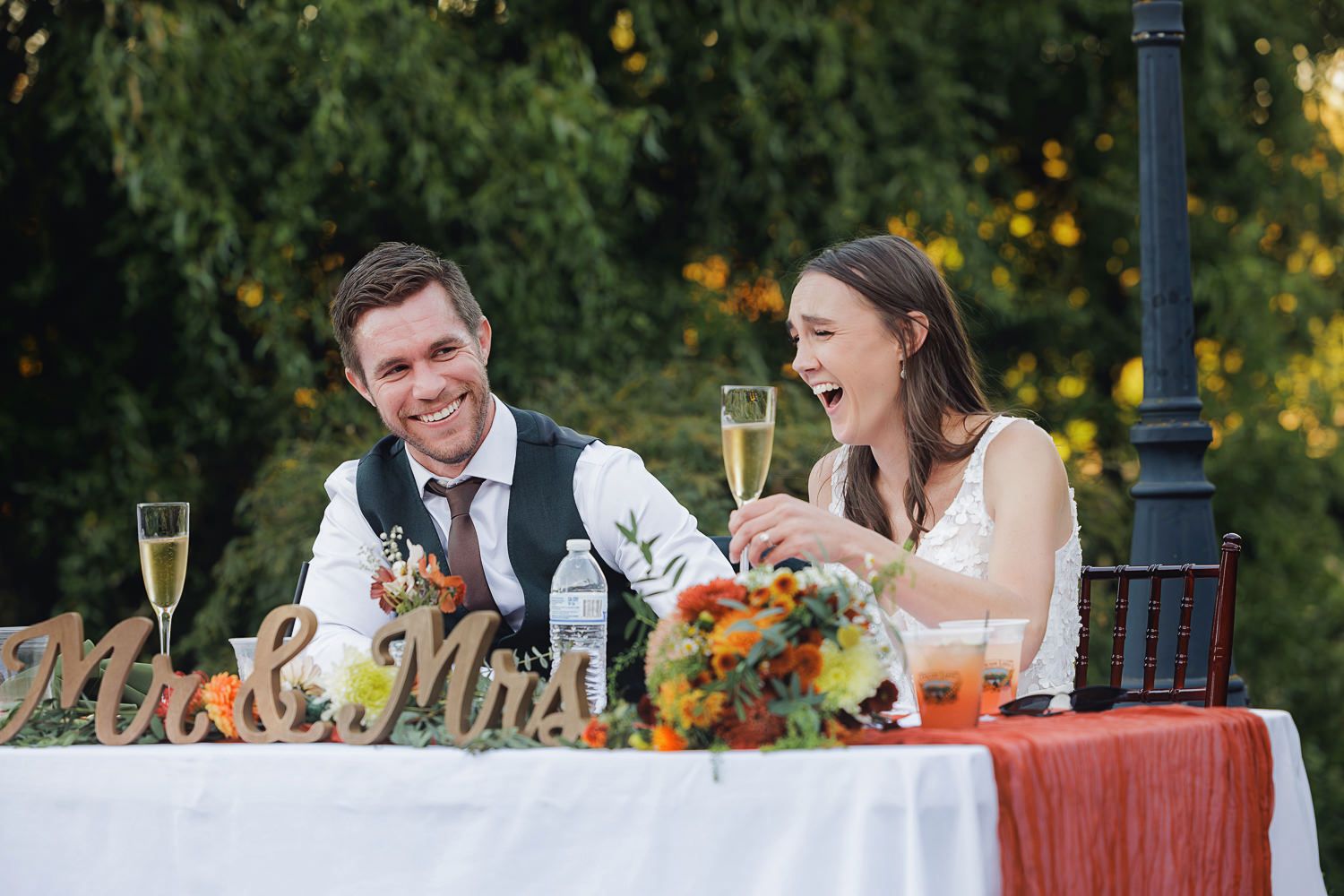 Wedding guests enjoy a festive outdoor reception dinner at a long table decorated with floral centerpieces.