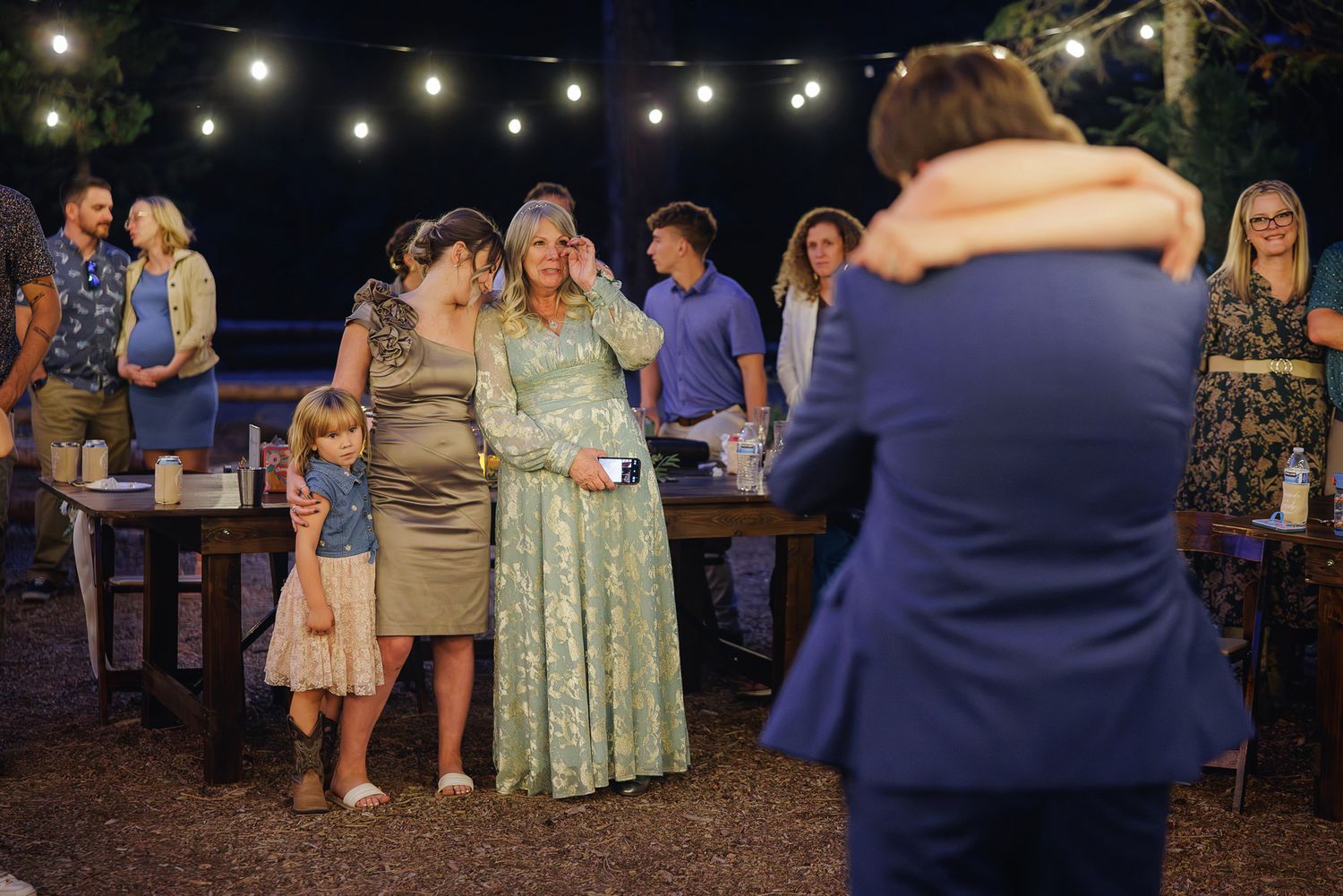 String lights illuminate an outdoor evening celebration with people gathered in a casual party setting.