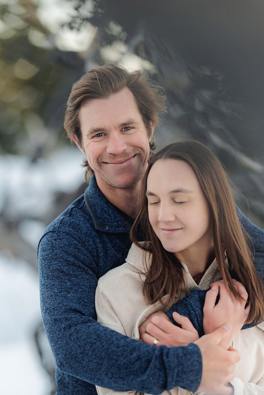 A romantic winter engagement photoshoot showing tender moments between a couple in warm sweaters against snowy backdrop.