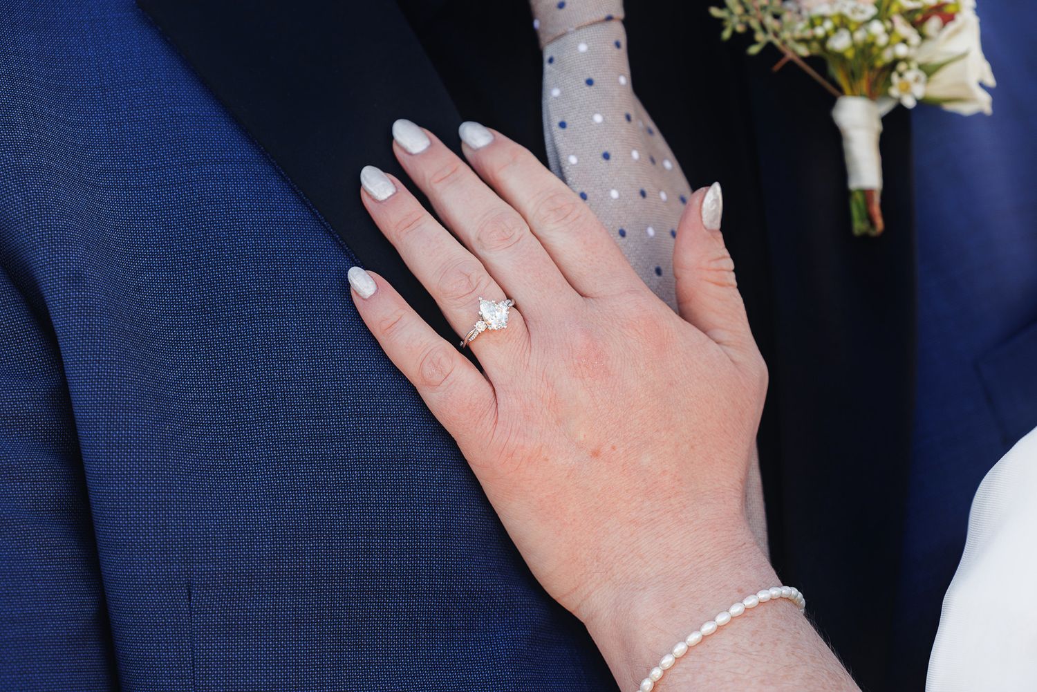 A close-up view of hands showing off engagement rings and wedding bands against a navy blue background.