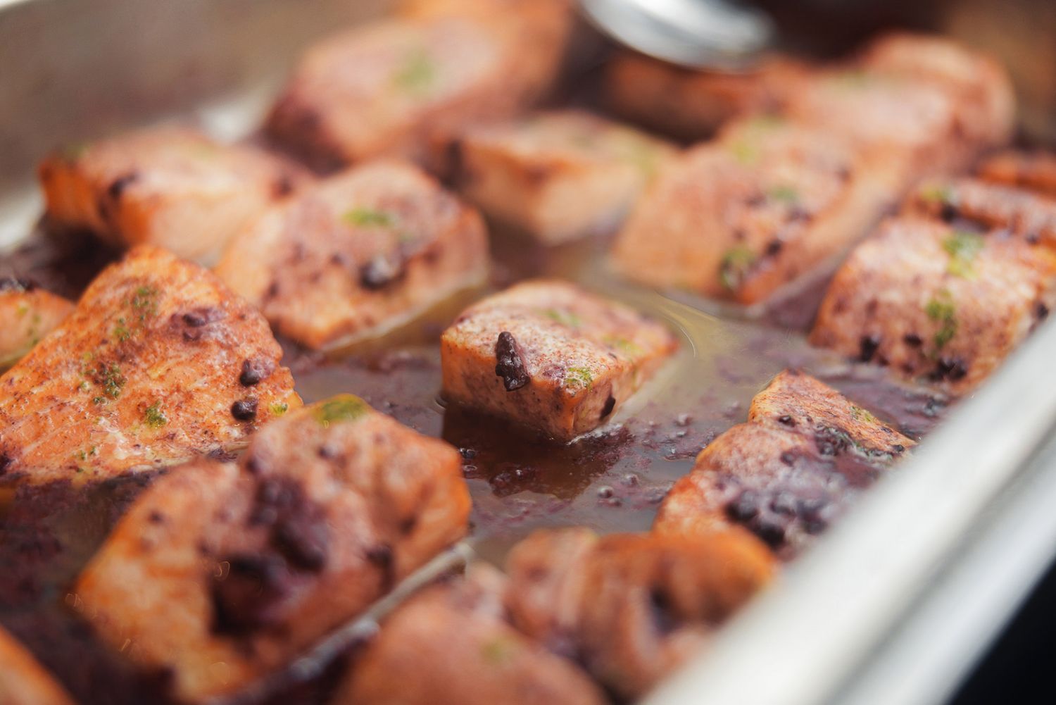 Grilled salmon fillets with crispy charred edges cooking on a metal baking sheet.