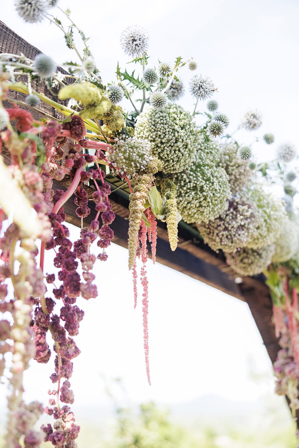 Elegant floral decor with cascading white and burgundy flowers hanging against a bright outdoor backdrop.