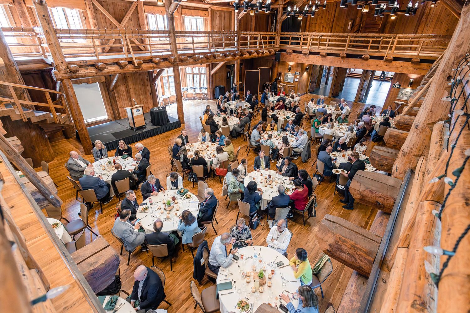 High angle view of a formal dining event in a timber-framed rustic venue with round tables.