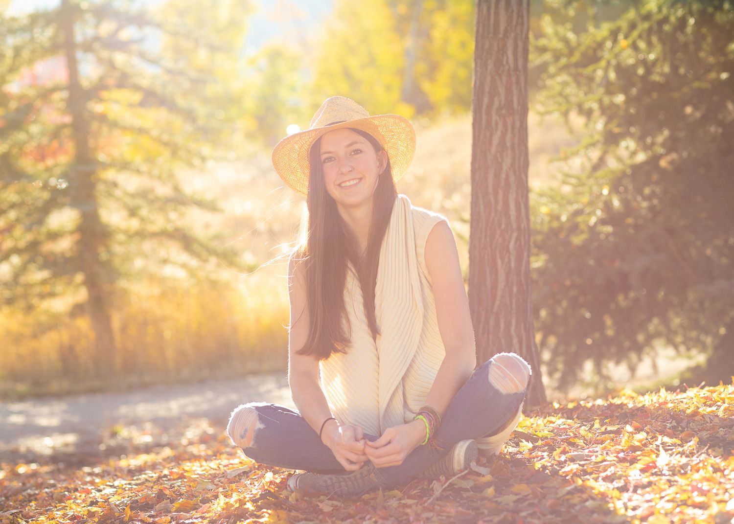 Person wearing straw hat sitting cross-legged in sunlit forest setting.