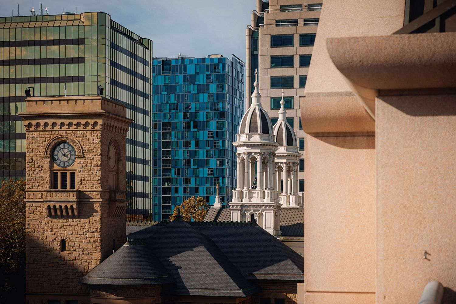 Urban architecture contrasts old and modern buildings with church spires against blue glass tower in downtown cityscape.