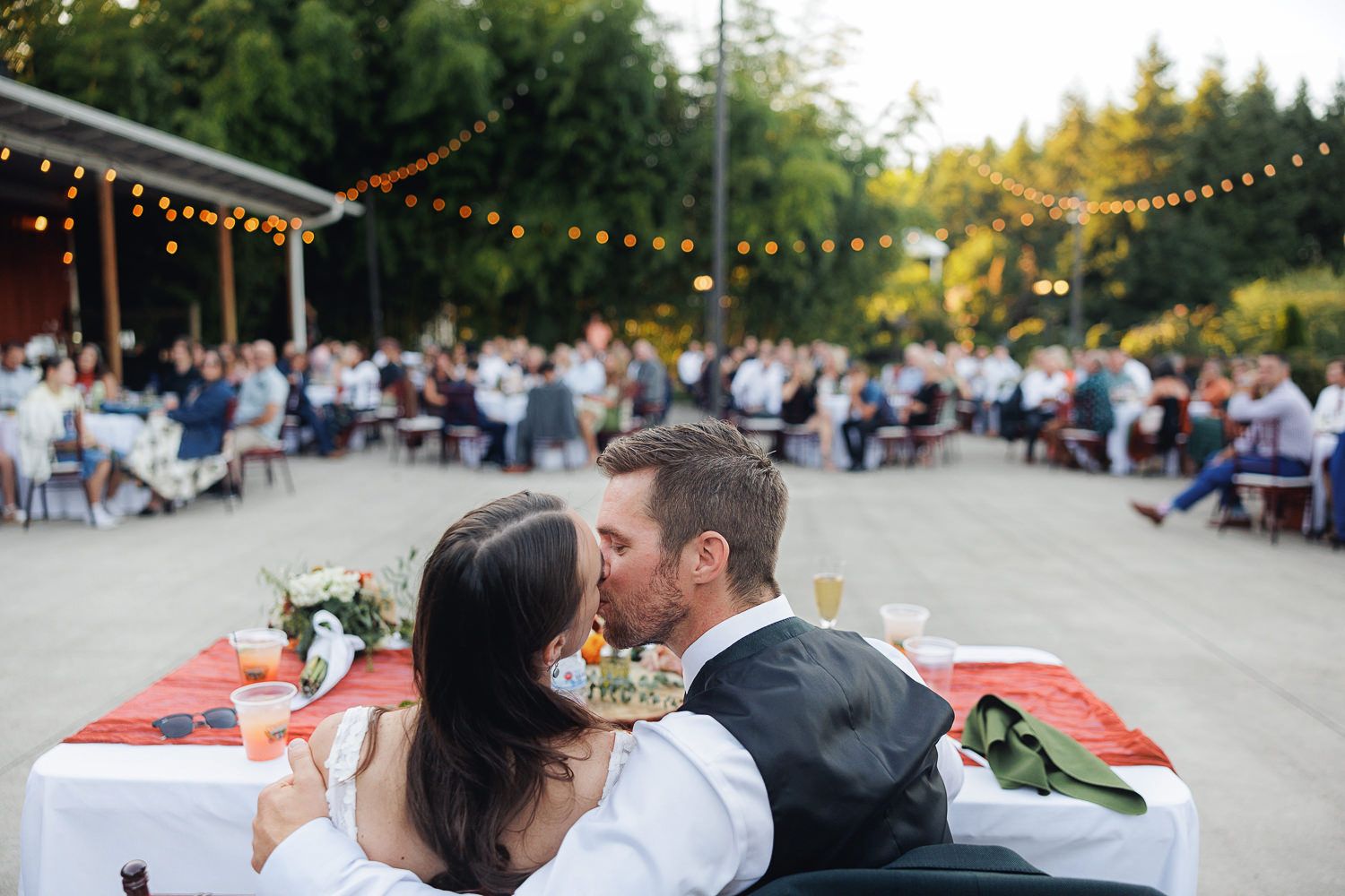 String lights illuminate an outdoor evening celebration with tables and guests gathered for a festive occasion.