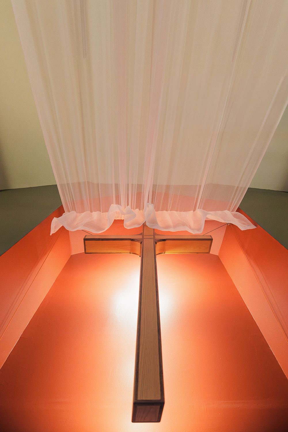 A wooden cross illuminated in orange light with flowing white fabric draping above it in a dramatic display.