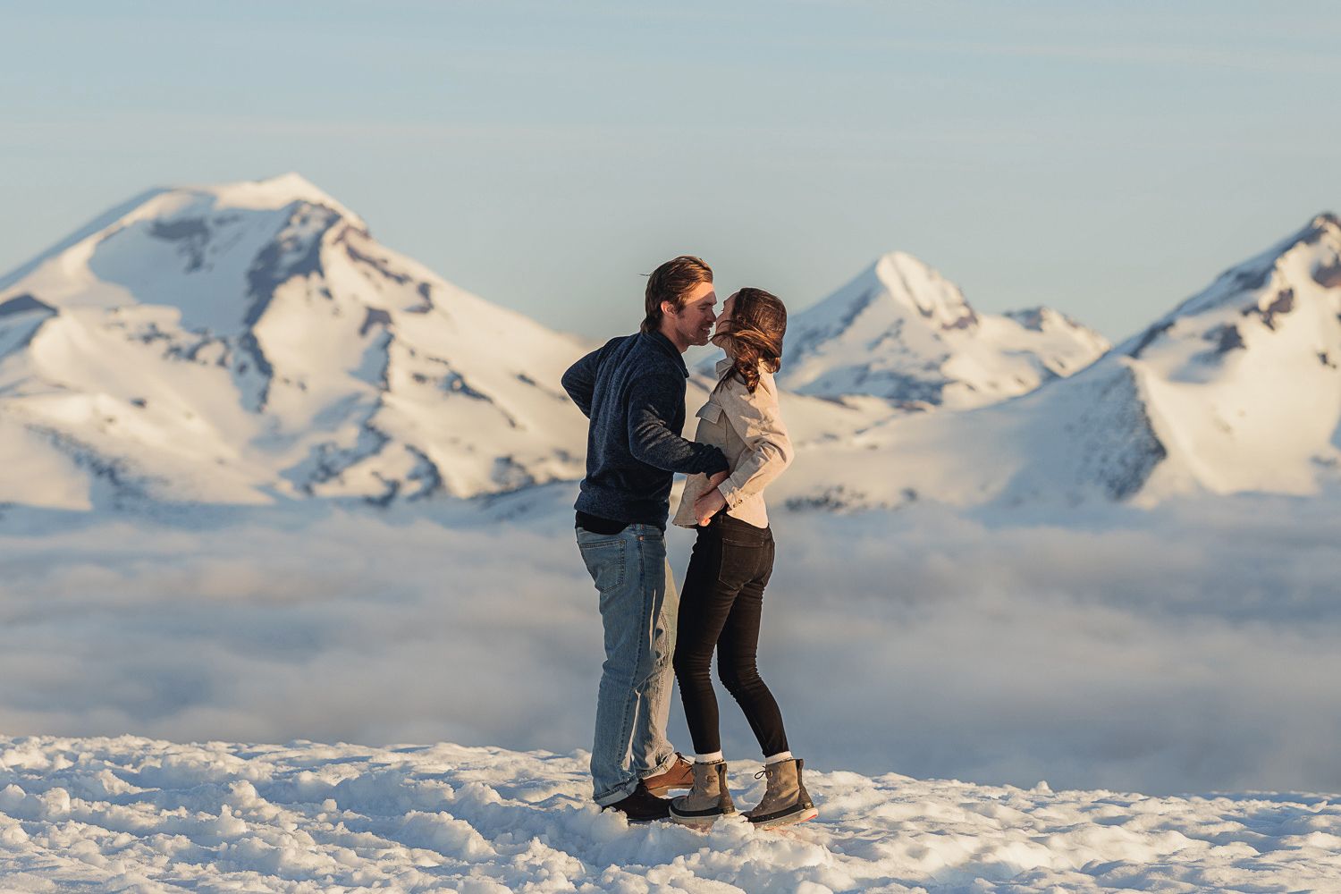 Two people share a romantic moment against a backdrop of snowy mountain peaks and clouds.