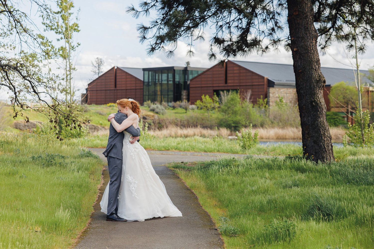 Bride and groom share a romantic kiss on a garden path surrounded by lush greenery and a rustic barn venue.