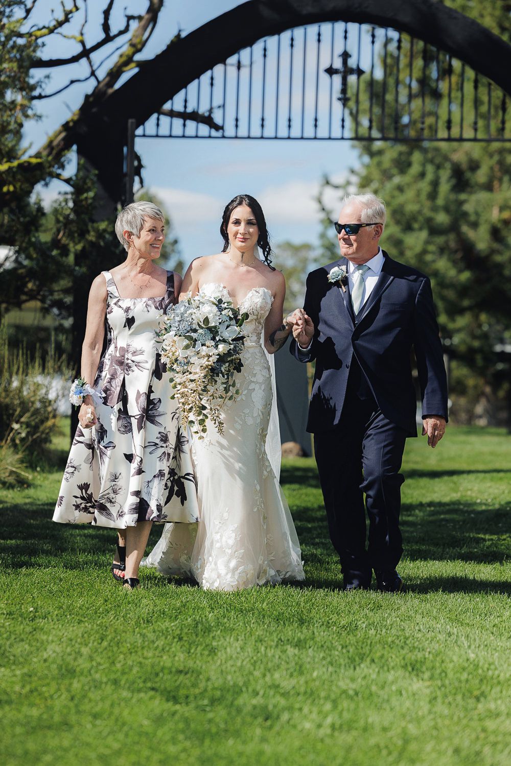 A beautiful wedding processional on a grassy lawn with an ornate iron gate arch visible in the background.