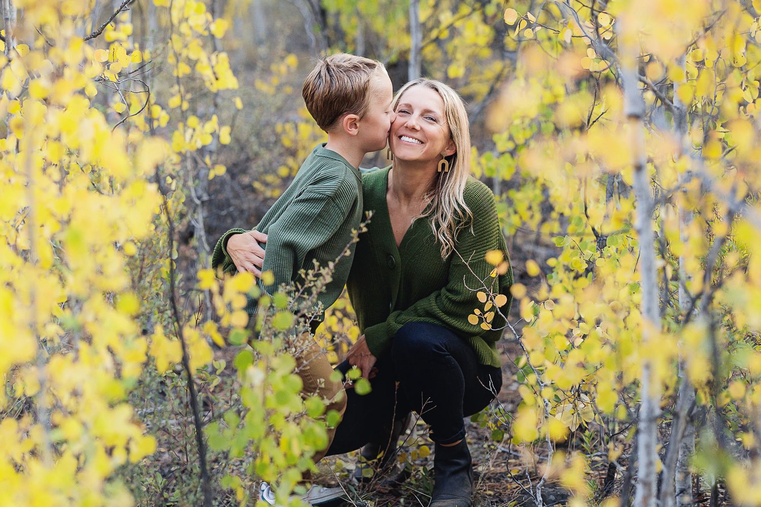 A happy couple in green sweaters share a joyful moment surrounded by blooming yellow forsythia branches in spring.