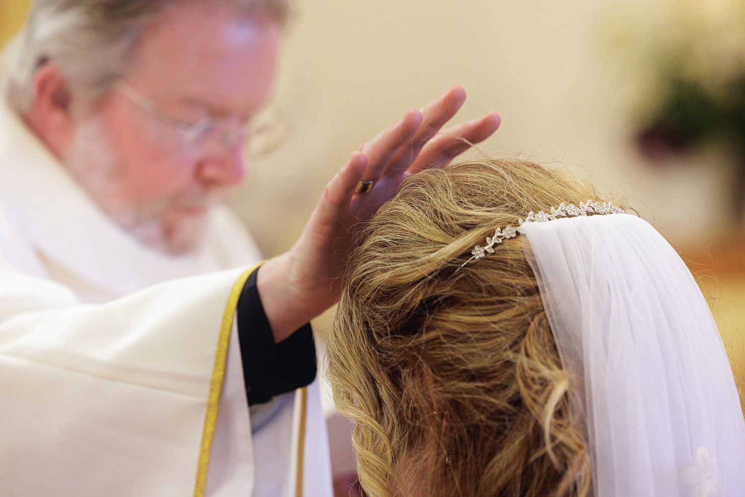 Priest blessing a bride during a wedding ceremony in a church, placing hand over her veiled head.