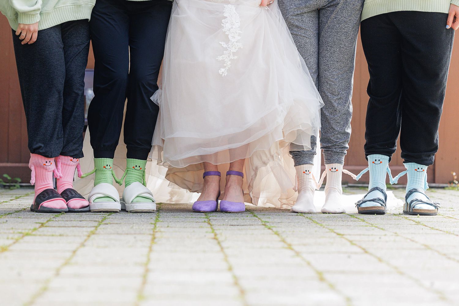 Bride and bridesmaids showing off colorful mismatched socks and shoes at a wedding ceremony outdoors.