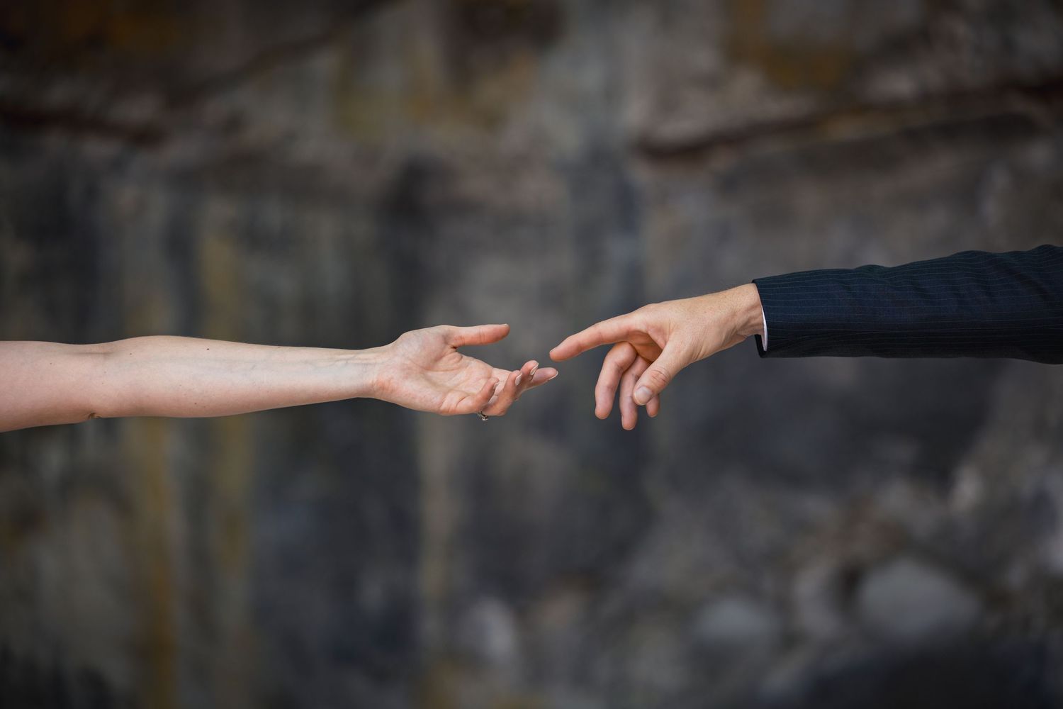 Two hands reaching towards each other with outstretched fingers against a blurry dark background.