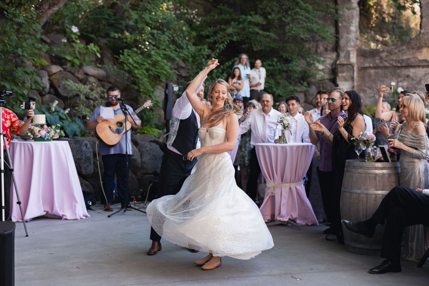 A couple dances at an outdoor wedding reception while guests look on and musicians perform in the background.