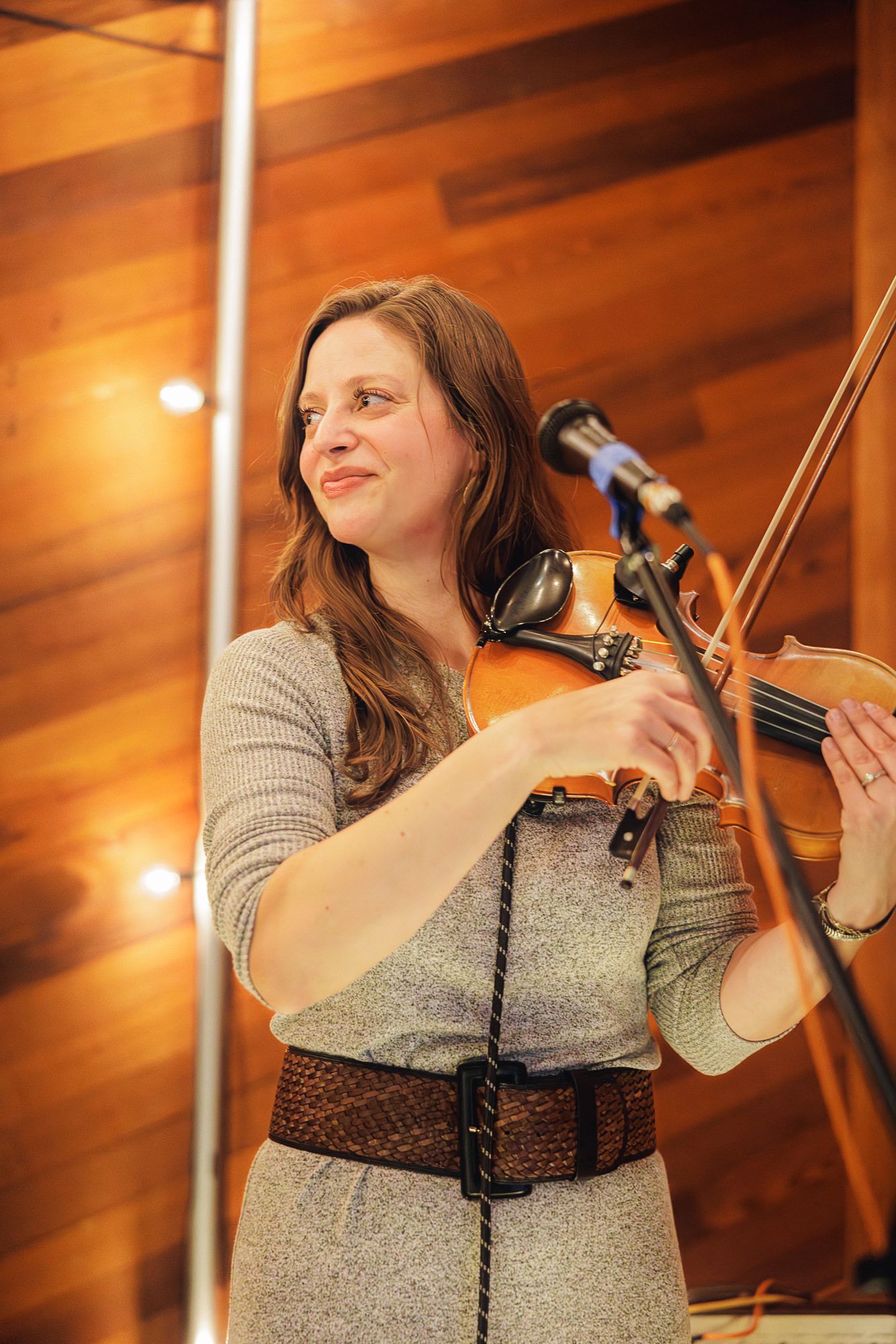 Musician performs passionately on violin against warm wooden backdrop in concert hall setting.