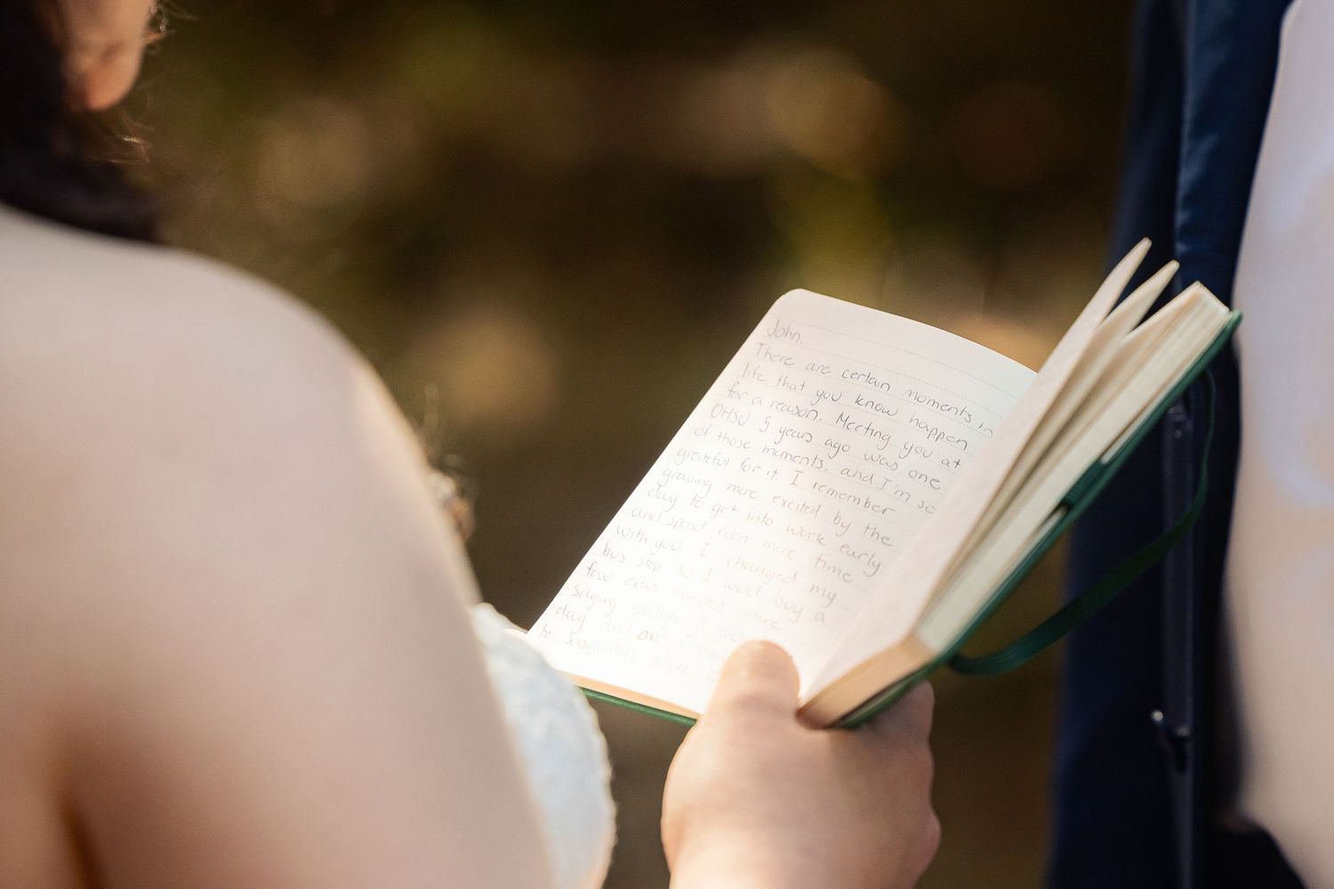 Someone holds an open book outdoors in natural lighting, with pages showing text visible in their hands.
