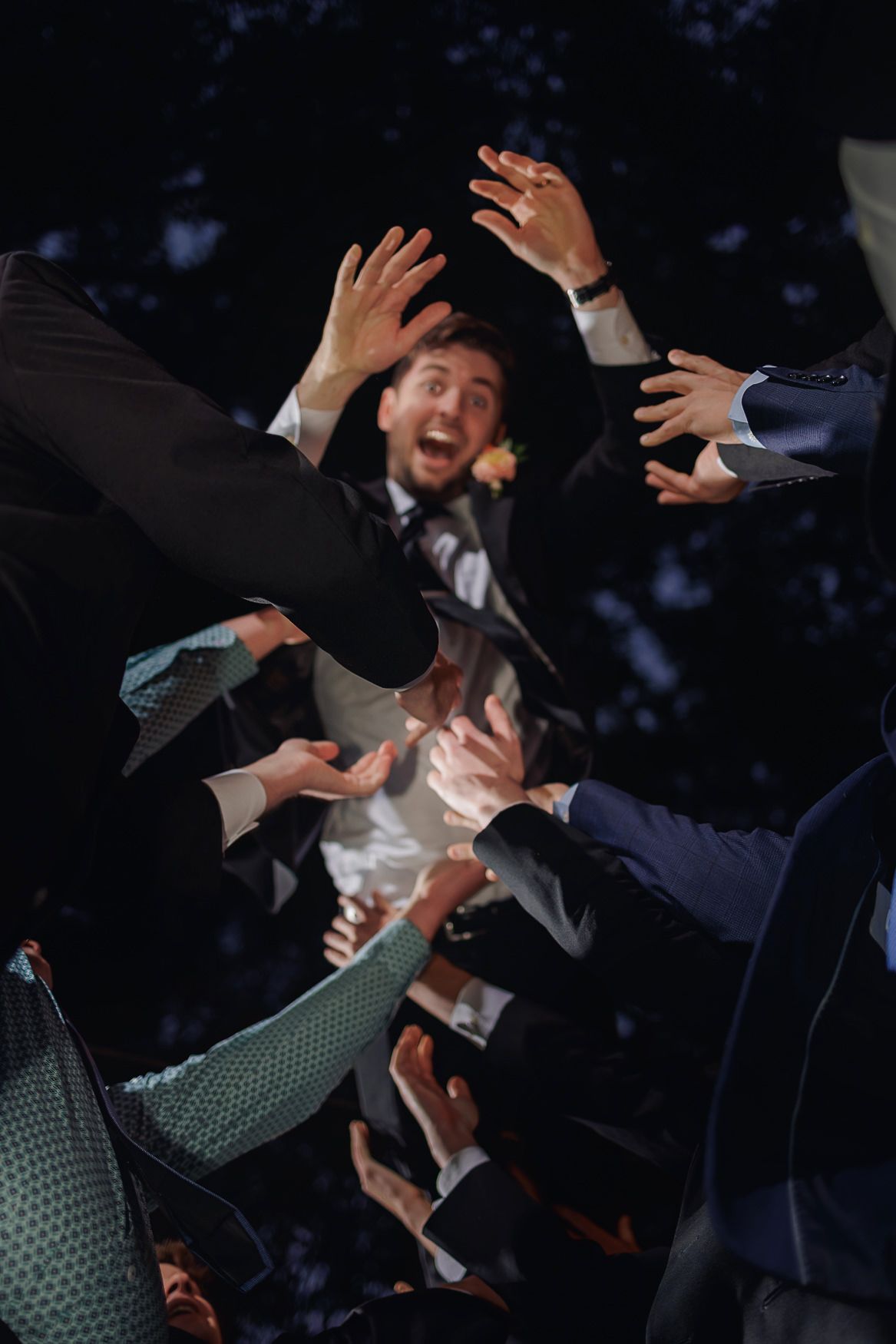 Wedding guests' hands reaching up to catch the bouquet being tossed in the air during a celebration.