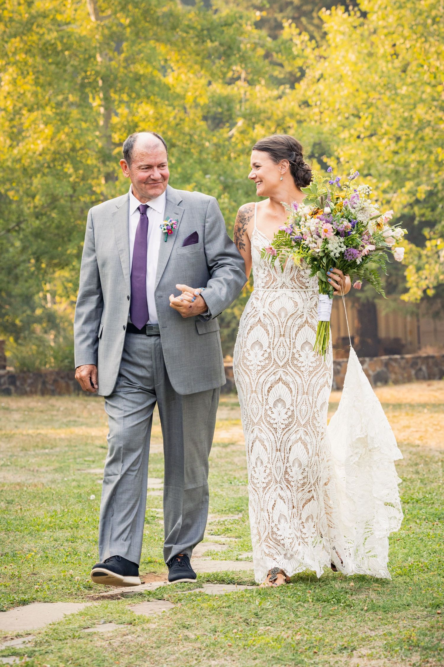 A couple walks along an outdoor path surrounded by yellow autumn foliage on their wedding day.