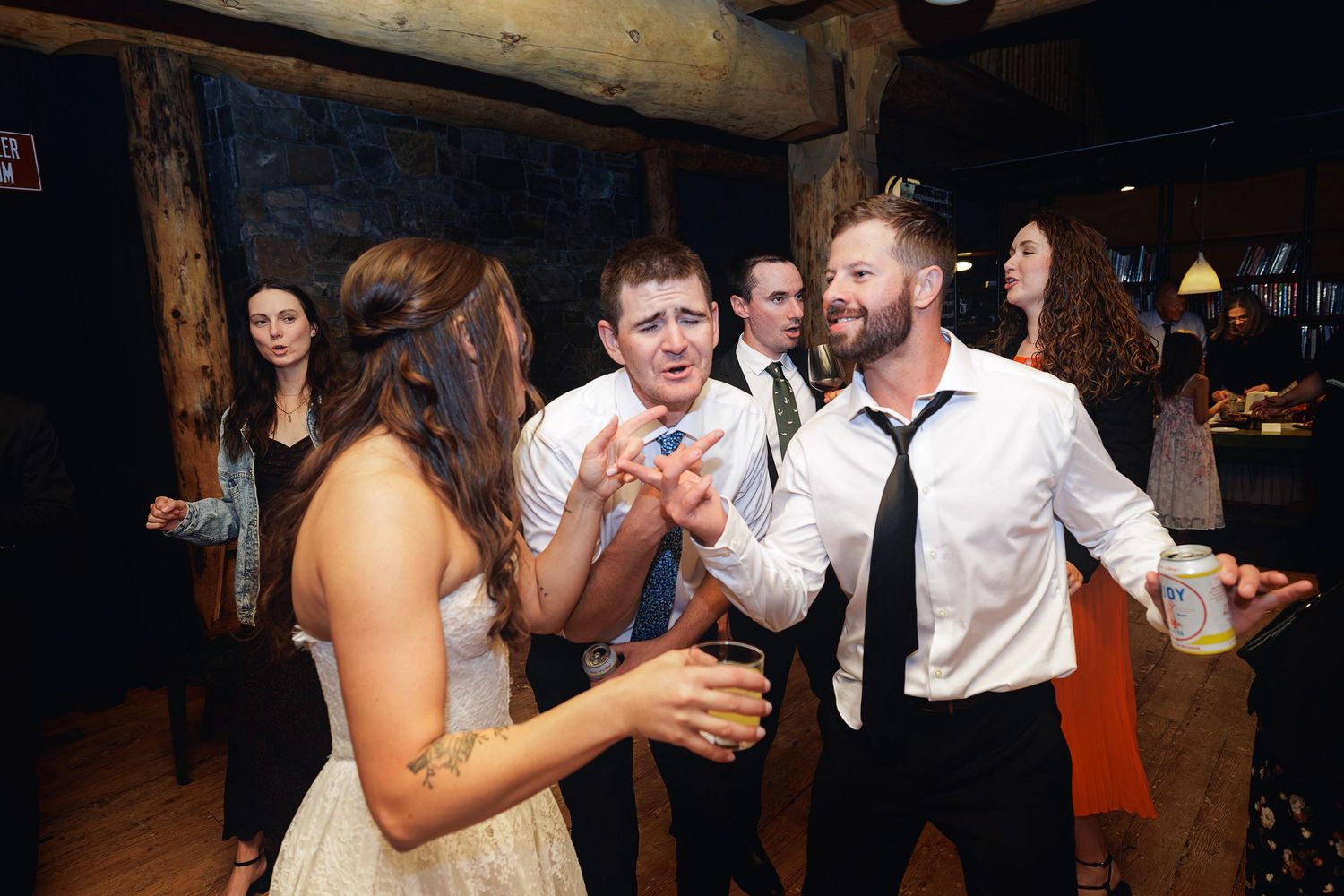Group of guests dancing and socializing at a rustic indoor wedding reception party.
