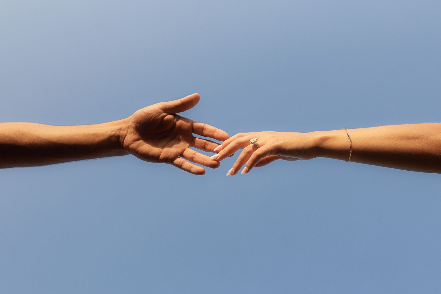 Two hands reaching toward each other against a clear blue sky, symbolizing connection and unity.