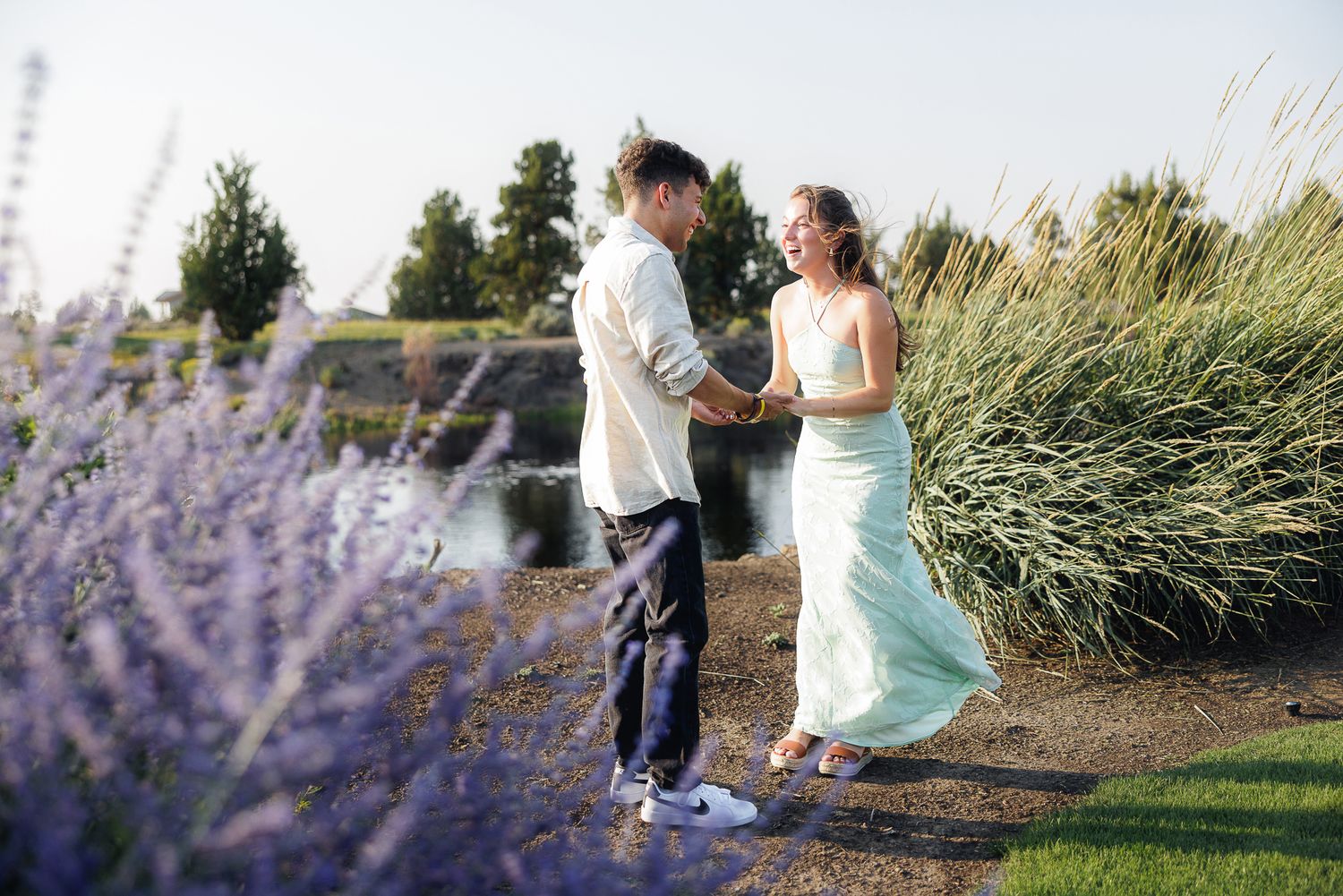 Couple holding hands in a garden with purple lavender flowers and tall grasses during golden hour outdoor engagement photo.