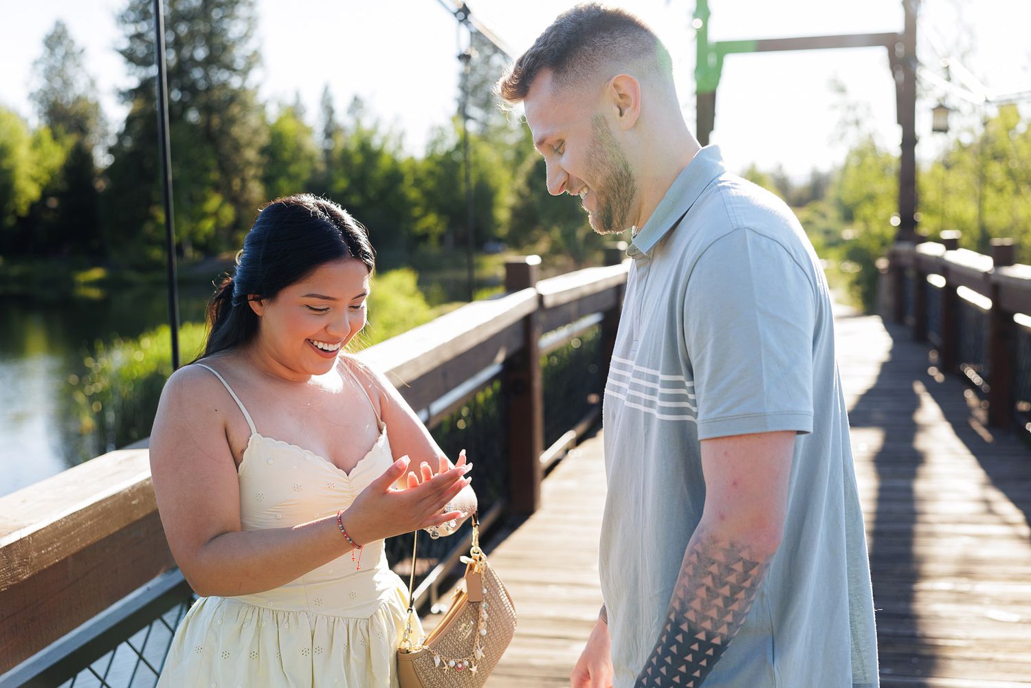 Couple sharing a joyful moment on a wooden bridge surrounded by lush greenery on a sunny day.