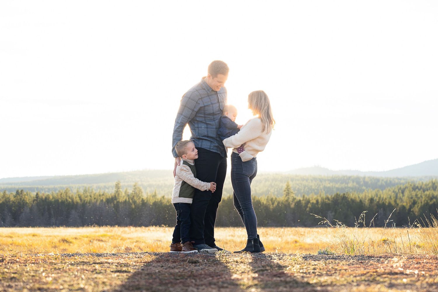 A couple stands together on a hill overlooking golden fields at sunset during a romantic outdoor moment.