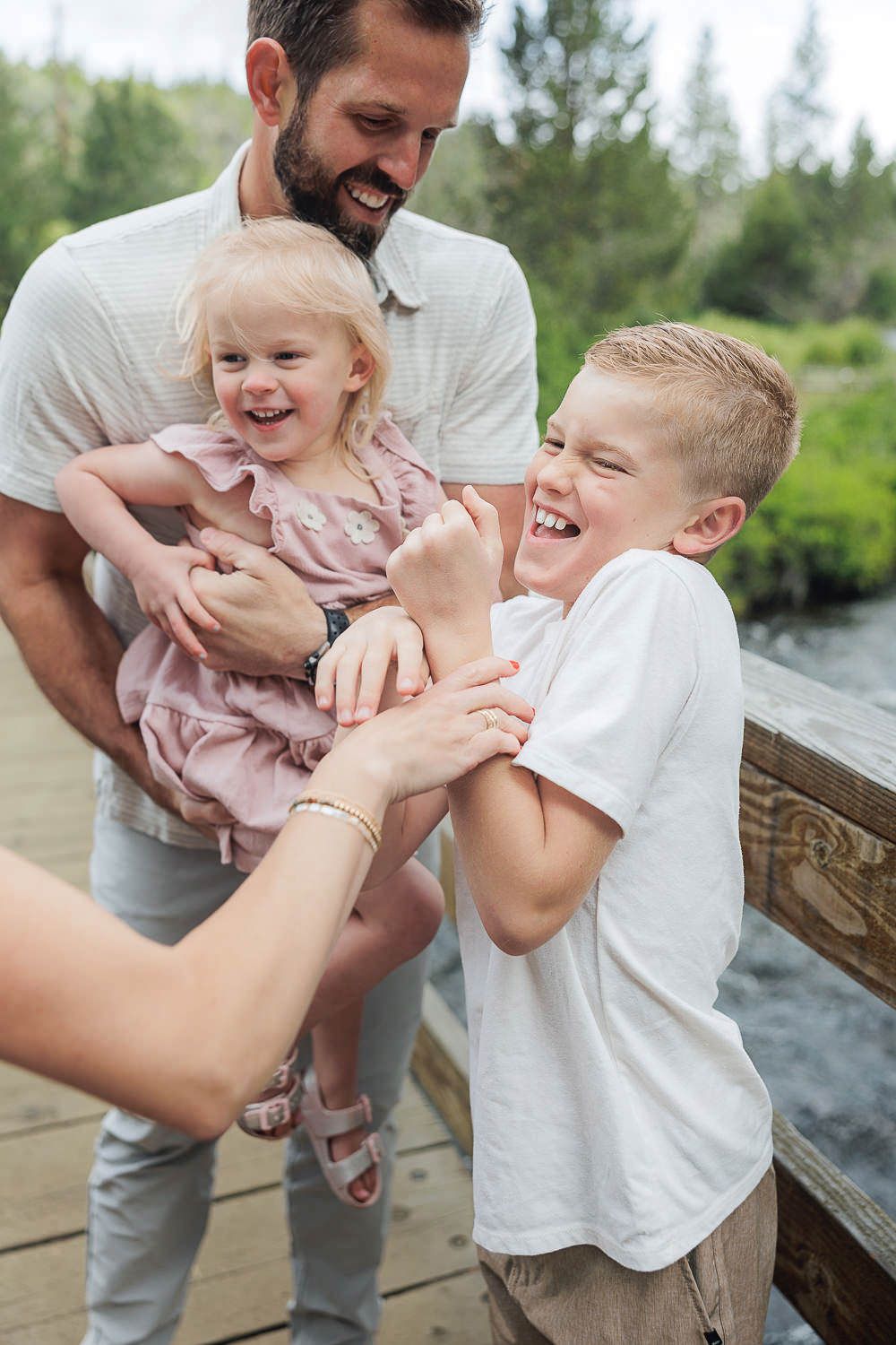 Family sharing joyful laughter together on wooden deck by river during outdoor summer photo session.