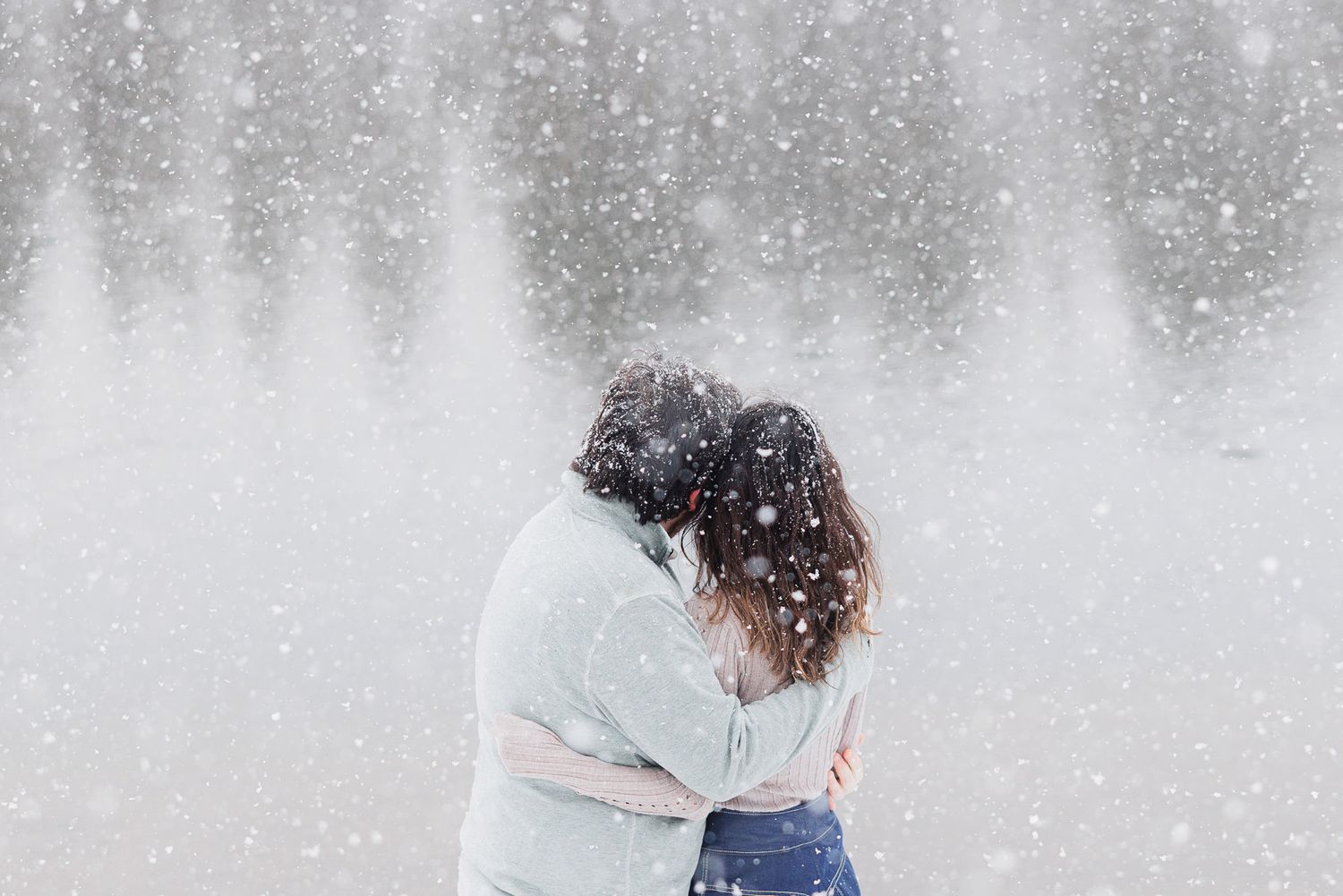 A person in a winter coat stands in falling snow against a blurry white background.
