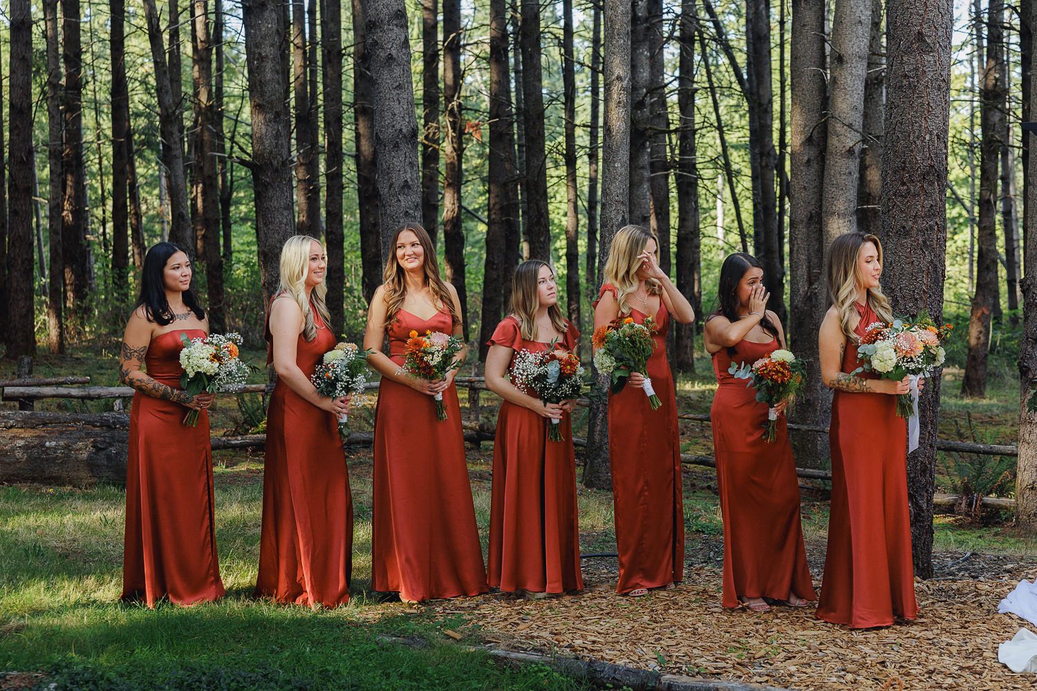 A group in matching orange dresses poses in a forest setting during an outdoor photo session.