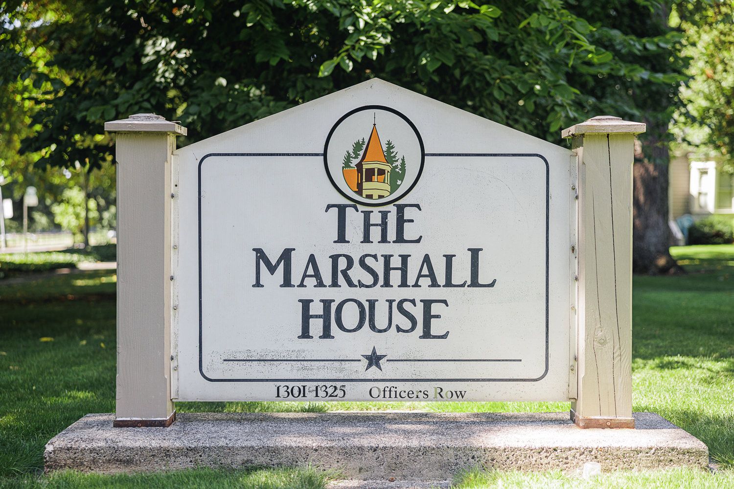 White wooden signs displaying 'The Marshall House' text mounted on stone pillars along a pathway with green foliage.