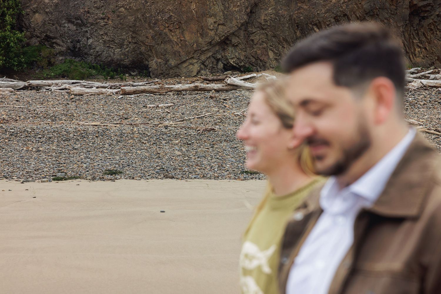 Couple sharing a romantic moment on a sandy beach with rocky cliffs in the background.